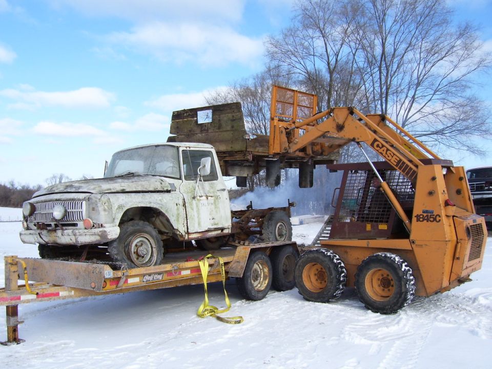 White pickup truck on trailer with skid steer loader, front 3/4 view