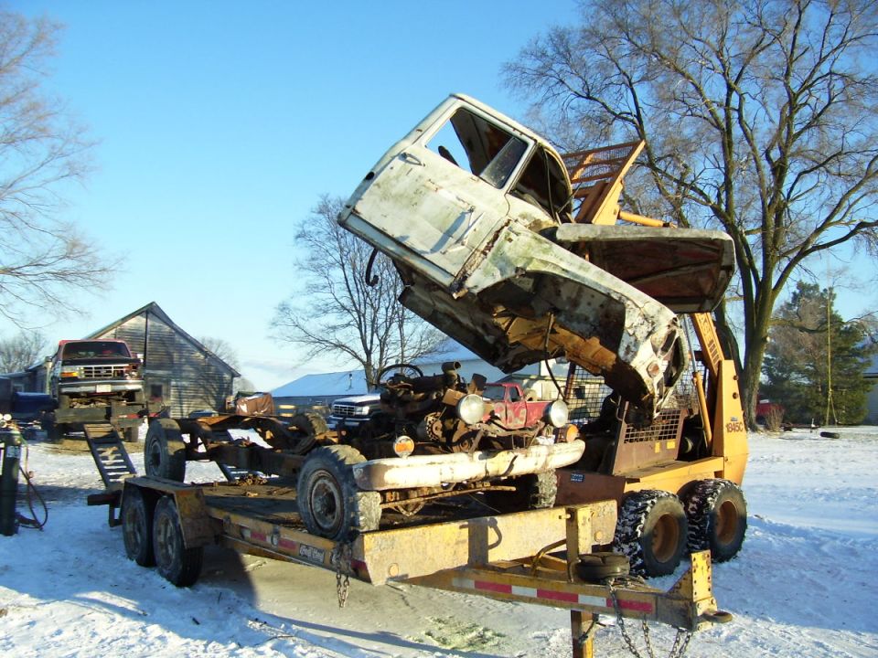 truck cab being lifted off chassis on trailer, another truck on flatbed in background