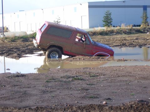1986 Ford Bronco - This red 1980s Ford Bronco is stuck deep in a muddy puddle, with its front end submerged.
