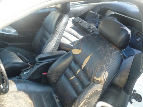1996 Ford Mustang - The interior of a car shows heavily damaged black leather seats and a disassembled center console.