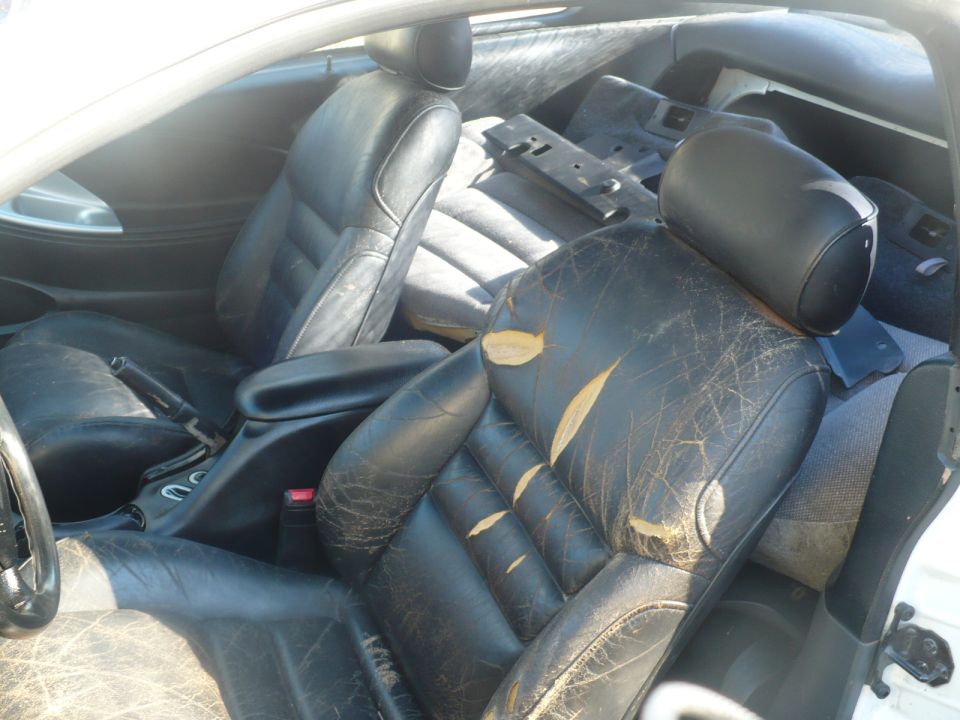 Interior of a worn black leather car seat with rips and tears, showing the center console and dashboard