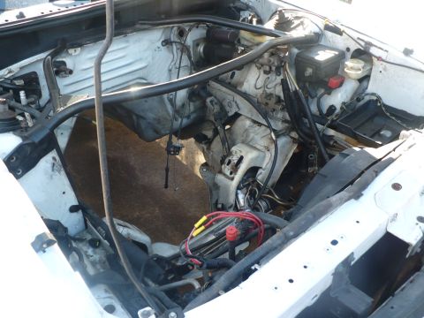 1996 Ford Mustang - The engine bay of a white vehicle appears to be undergoing repairs or has had its engine removed, revealing exposed wiring and components.