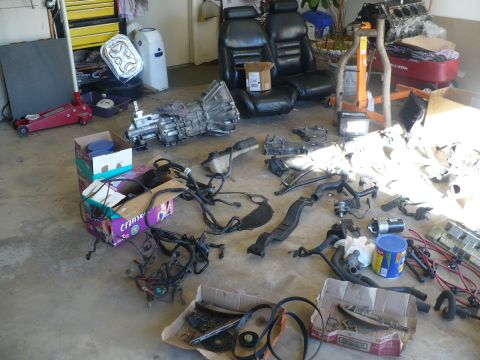 1996 Ford Mustang - Disassembled car parts and interior seats are spread across a garage floor.