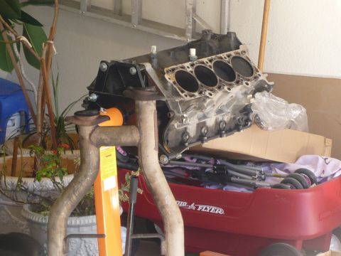 1996 Ford Mustang - An engine block and exhaust system are shown, disassembled and on a stand, with various parts in a red wagon.