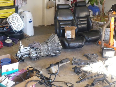 1996 Ford Mustang - Various car parts, including a transmission and seats, are laid out on a concrete floor in a garage.