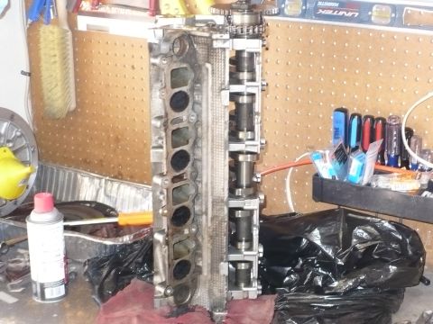 1996 Ford Mustang - Engine cylinder head with camshafts and intake ports visible, resting on a workbench.