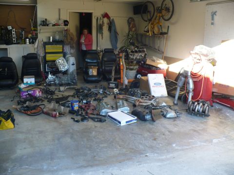 1996 Ford Mustang - A collection of automotive parts and interior seats are laid out on the concrete floor of a garage.