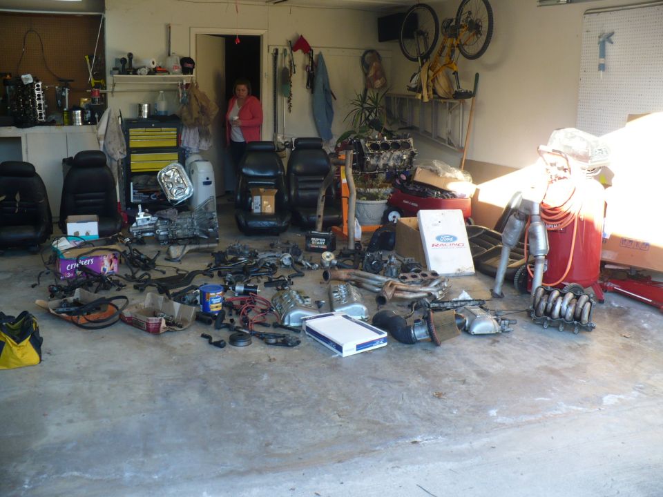 Car seats, engine parts, exhaust, and an air compressor are spread out on a garage floor