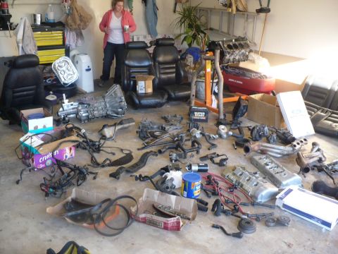 1996 Ford Mustang - A collection of car parts and seats are laid out on a garage floor, with a woman standing in the background.
