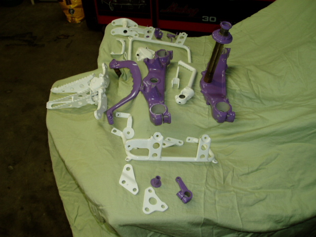 Various motorcycle parts, some painted purple and white, laid out on a green tarp