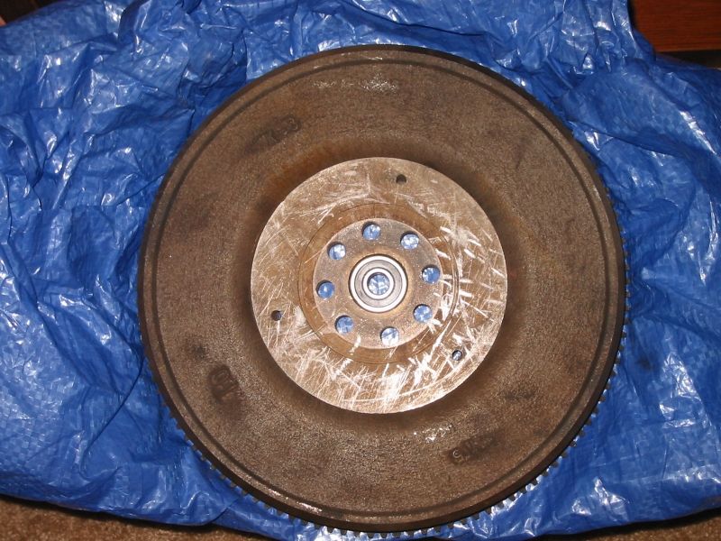 Used flywheel on a blue tarp with ring gear teeth, pilot bearing and eight hub bolts