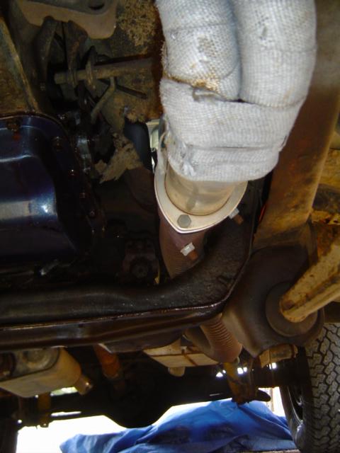 1979 Ford Bronco - Underbody view looking up at an exhaust manifold flange and header pipe wrapped in white heat wrap, routed past a painted oil pan, frame ra…