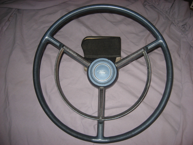 Vintage Ford steering wheel with chrome horn ring and blue Ford center cap lying on fabric