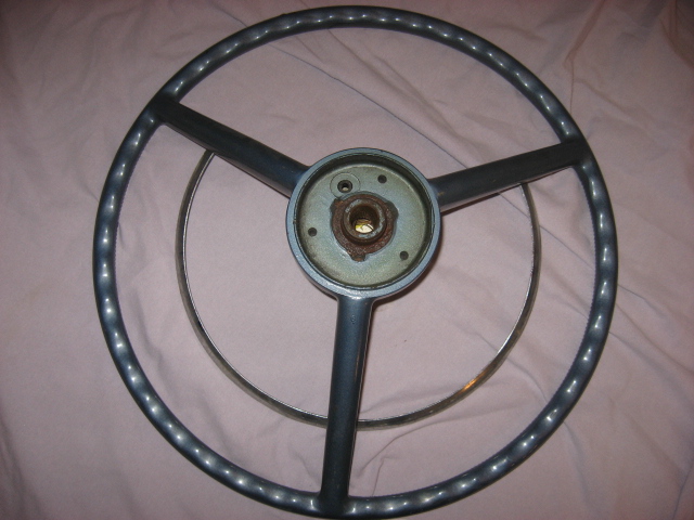 Gray steering wheel with three spokes and a chrome ring, on a pink fabric surface