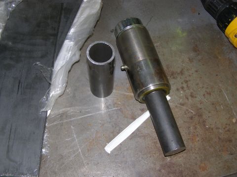 1993 Ford Bronco - A metal pipe and a hydraulic cylinder are shown on a workbench next to some sheet metal.