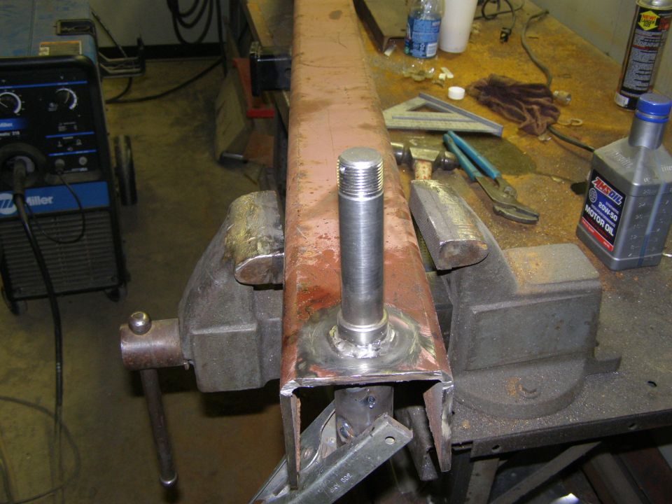 Metal tube clamped in a vise with a threaded rod welded to it. Miller welder and Amsoil motor oil visible in background
