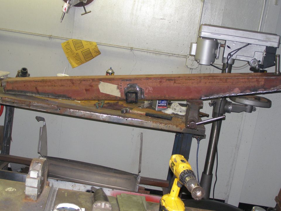 Metal beam with a hitch receiver welded on, clamped in a vise on a workbench next to a drill press