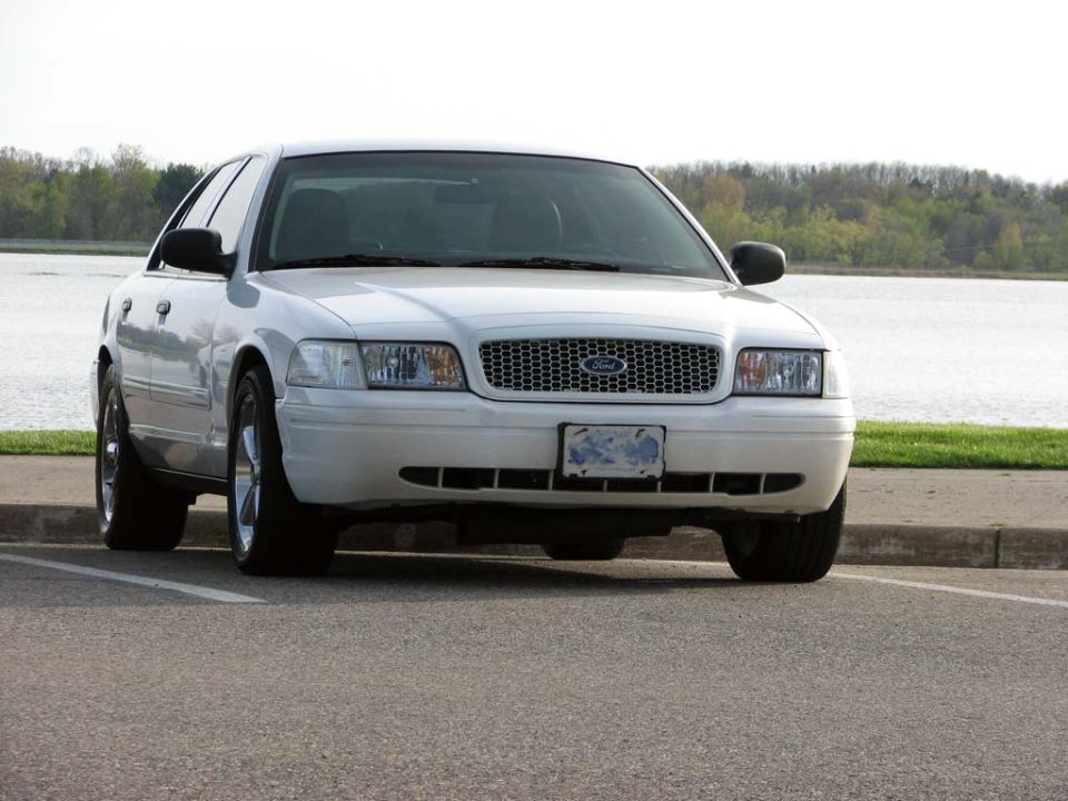 White Ford Crown Victoria sedan front 3/4 view parked by a lake, mesh grille and alloy wheels