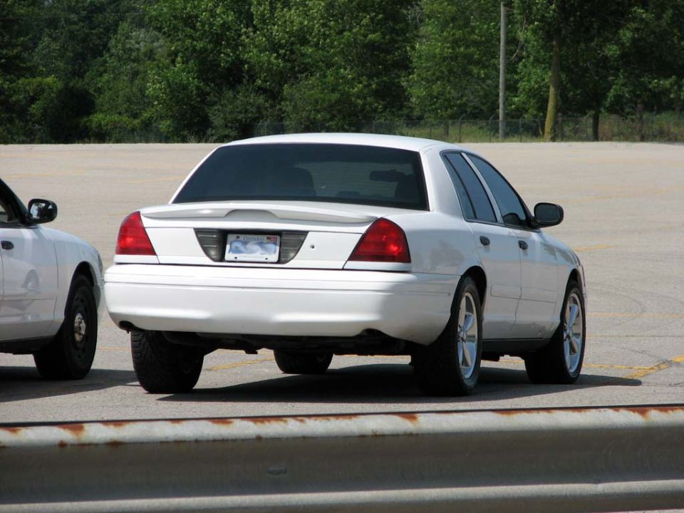 White Ford Crown Victoria sedan rear 3/4 view with spoiler and silver five-spoke wheels
