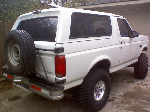 1995 Ford Bronco - White 1995 Ford Bronco with a lifted suspension and large tires, seen from the rear three-quarter view.