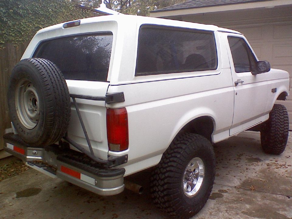 1995 Ford Bronco, rear 3/4 view, white, lifted with large off-road tires, spare tire mounted on rear door