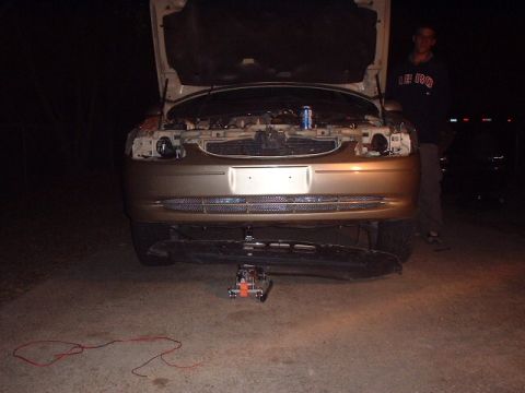 2000 Ford Taurus - Front view of a gold sedan with its hood open, being worked on with a jack underneath the bumper.