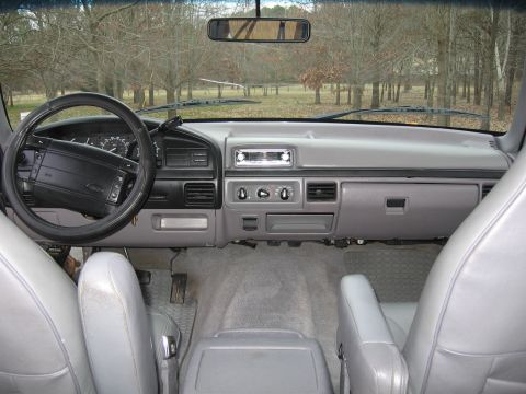 1967 Ford Mustang - The interior of a Ford Bronco shows a gray dashboard, steering wheel, and seats, with trees visible through the windshield.