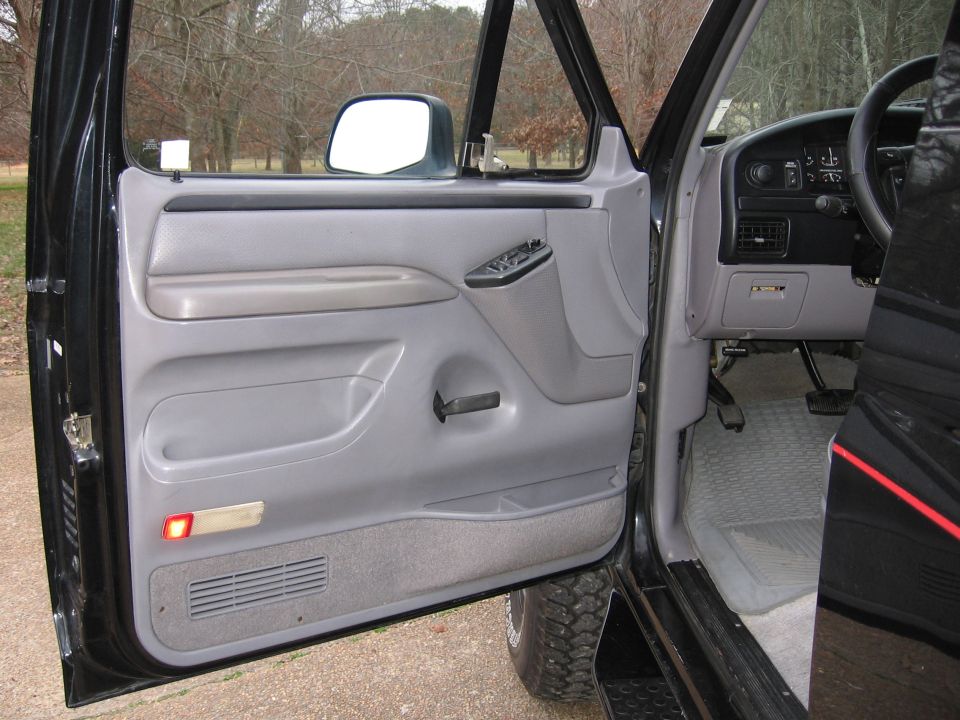 Interior of black truck, driver's door open. Shows door panel, dashboard, steering wheel, and floor mats