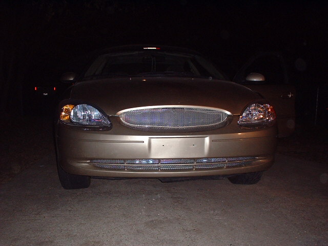 Gold 2000 Ford Taurus front view, aftermarket grille, dark background