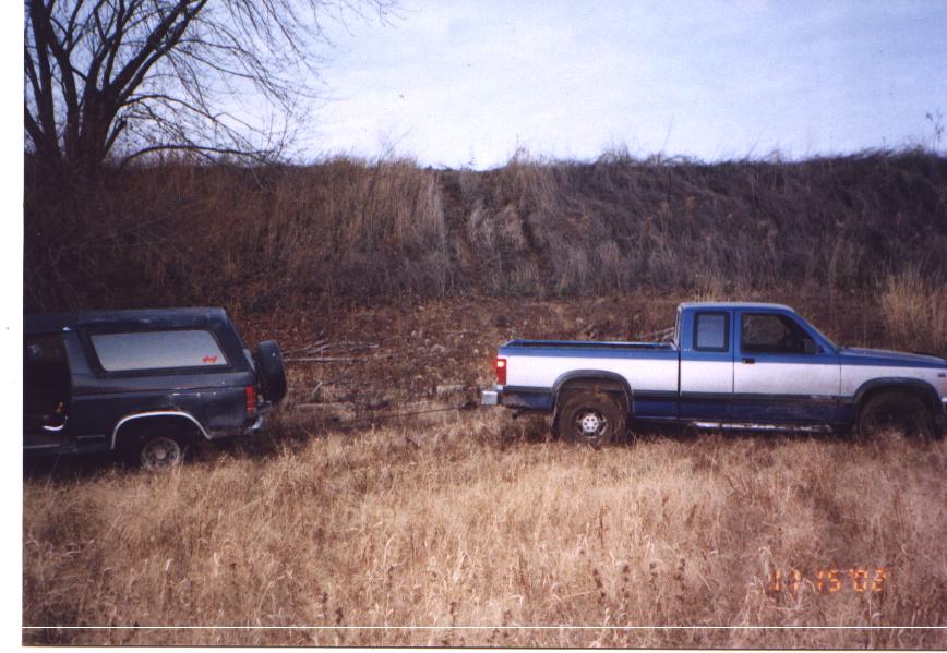 Dark blue Ford Bronco towed by a blue and silver pickup with a strap in tall dry grass