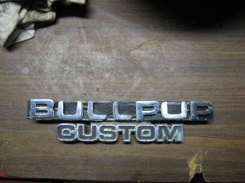 1979 Ford Bronco - Emblems reading BULLPUP CUSTOM are shown on a wooden surface.