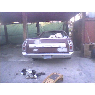 1972 Ford Ranchero - The rear of a 1972 Ford Ranchero is visible, parked under a cover with some items on the ground nearby.