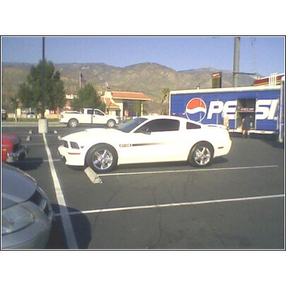 1972 Ford Ranchero - White Ford Mustang parked in a lot with a Pepsi trailer and mountains in the background.
