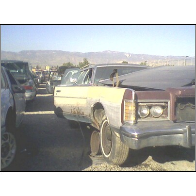 1972 Ford Ranchero - A collection of vehicles sit in a junkyard under a clear sky with mountains in the distance.