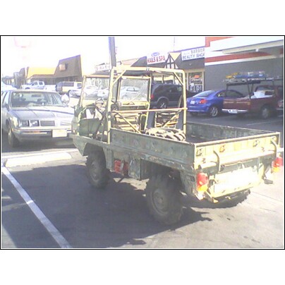1972 Ford Ranchero - A military utility truck is parked in a lot with other vehicles visible in the background.