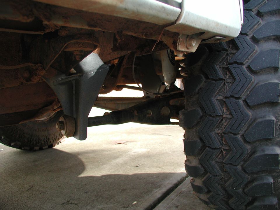 Underside of lifted truck showing black drop bracket, coil spring and axle