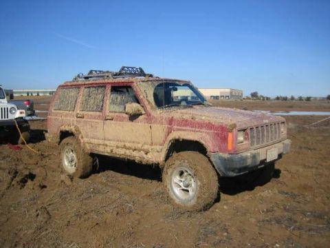 1986 Ford Bronco - A red Jeep Cherokee is stuck in the mud, with a white Jeep attempting to tow it out.