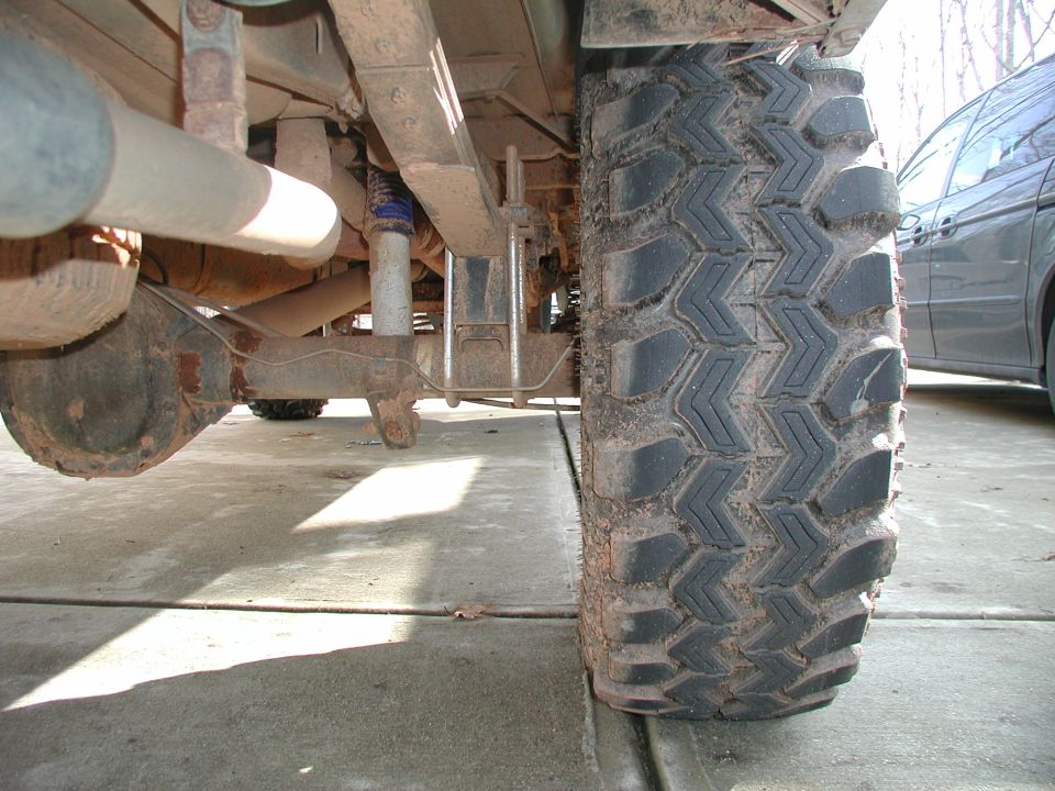 Under-truck view of a lifted pickup's rear axle, shock and exhaust beside a mud tire