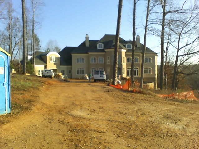 Construction site with a large house, two trucks, and a portable toilet