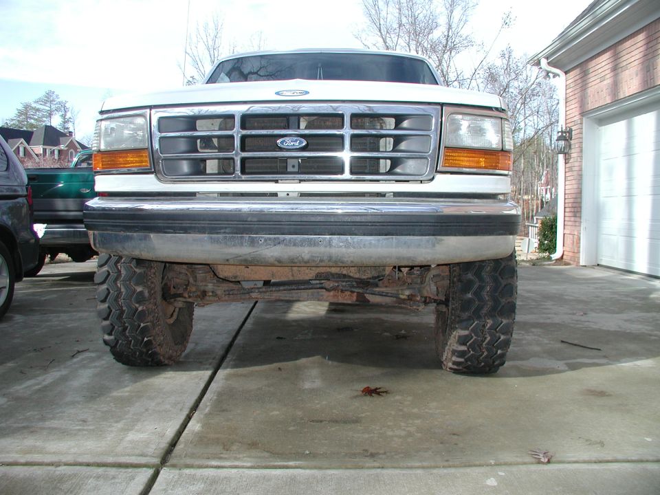 White lifted Ford truck head-on, showing chrome grille, front axle, and mud tires on a driveway