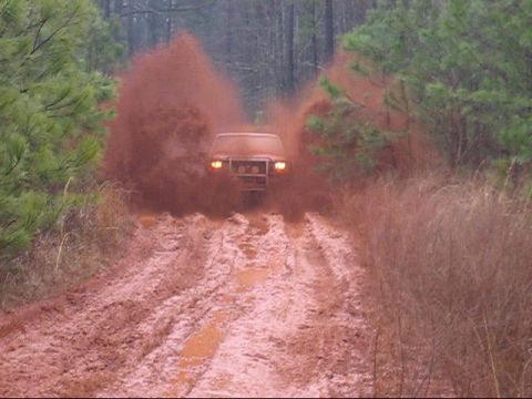 1996 Ford Bronco - Ford Bronco navigates a challenging muddy off-road path, creating a significant splash.