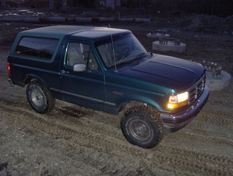 1996 Ford Bronco - This Ford Bronco is parked on a dirt lot with construction materials in the background.