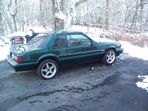 1991 Ford Mustang - A green 1991 Ford Mustang coupe is parked outside in a snowy environment, aftermarket wheels and 5.0 badging.