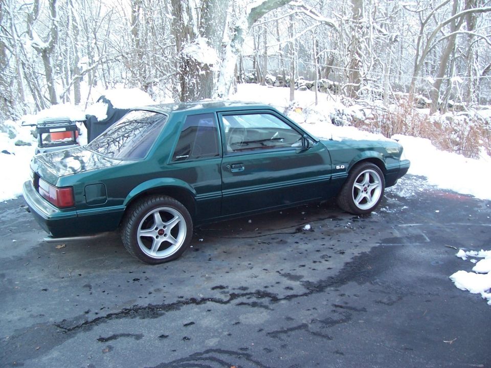 Green 1991 Ford Mustang coupe with 5.0 badging and aftermarket wheels in snow