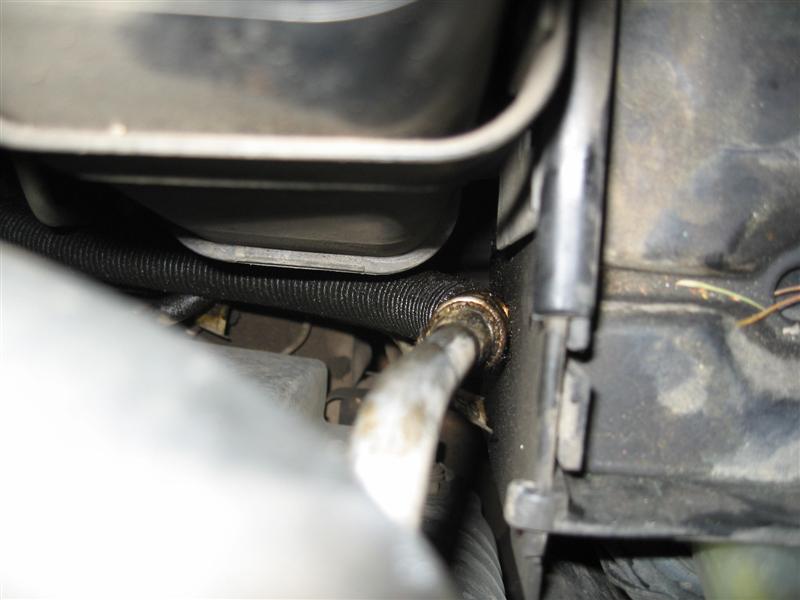 Close-up of a metal hose connected to a black corrugated tube, with engine components in the background