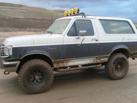 1989 Ford Bronco - This muddy Ford Bronco, equipped with auxiliary lights, is shown from a three-quarter front angle.