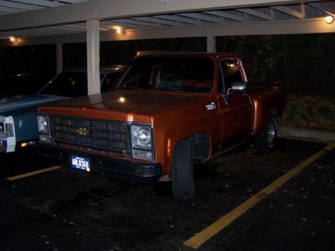 1979 Chevrolet C/K Pickup - This orange pickup truck is parked under a covered area, with another vehicle beside it.