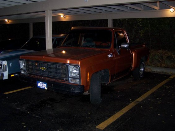 Orange 1979 Chevrolet C/K Pickup parked under a carport. Another vehicle is partially visible to the left
