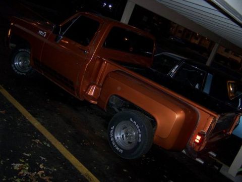 1979 Chevrolet C/K Pickup - An orange pickup truck is parked under a covered area at night.