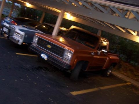 1979 Chevrolet C/K Pickup - This orange 1979 Chevrolet C/K Pickup truck is parked under a carport, with another vehicle visible behind it.